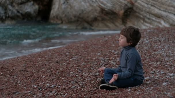 Lille dreng mediterer sidder ved havet udendørs . – Stock-video