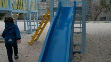 Küçük çocuk bir plastik slayt aşağı parkta serin günde rides.