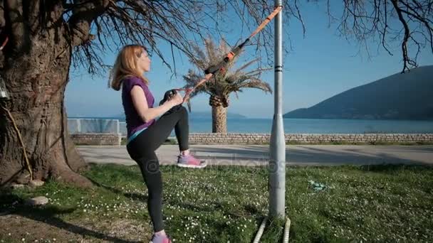 Jeune femme pratiquant des fentes avec des boucles TRX en plein air . — Video