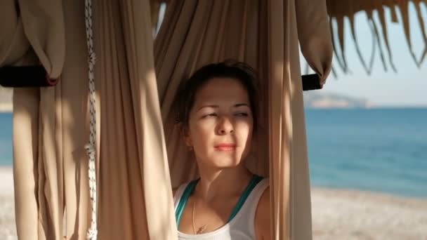 Op het strand, vrouw zit in een swingende hangmat en kijkt naar de afstand — Stockvideo