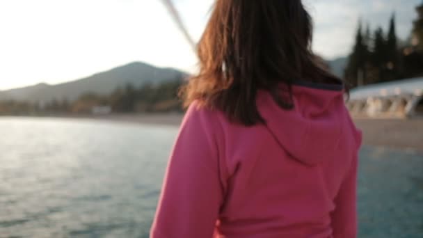 Una donna in giacca rosa è seduta al tramonto in riva al lago . — Video Stock