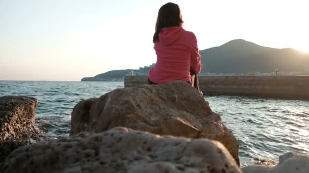 Bella bruna si siede sulle rocce vicino al lago nel suo viaggio . — Video Stock