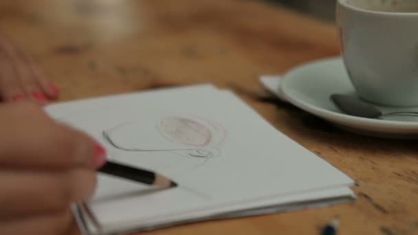 La mano de las mujeres dibuja una taza de lápiz y un platillo, que están sobre la mesa . — Vídeos de Stock