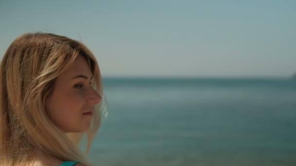Giovane donna attraente in piedi sulla spiaggia il giorno d'estate. Ammira distese sconfinate di oceano maestoso e guarda indietro con sorriso amichevole — Video Stock