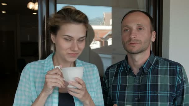 Young woman and man drinking tea standing on balcony indoors. — Stock Video