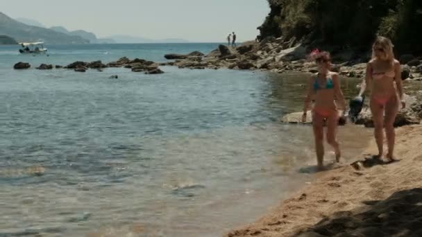 Zwei Frauen in Bikinis spazieren am öffentlichen Strand in der Nähe der Berge. — Stockvideo
