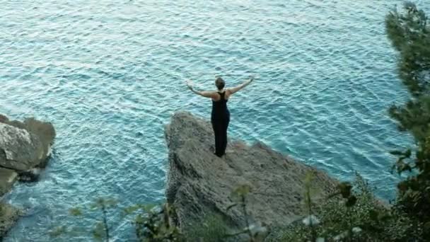 Mulher em uma rocha pela bela lagoa levanta as mãos . — Vídeo de Stock