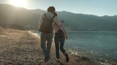 Çift sahilde akşamları dağların bir arka plan üzerinde yürüyor.