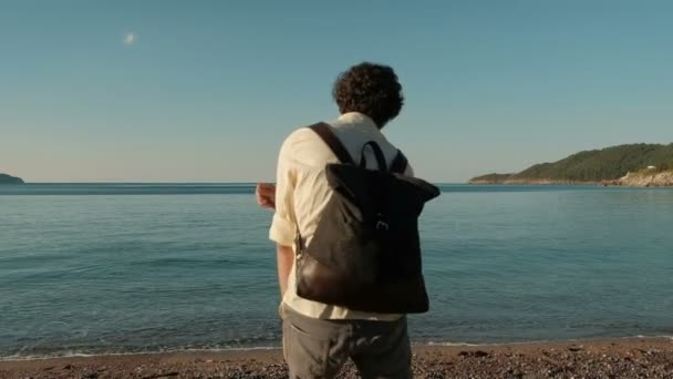 Молодий чоловік кидає плоский маленький камінь у море у своєму дозвіллі . — стокове відео