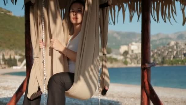 Mujer se sienta en una hamaca en una playa soleada y mira a la distancia . — Vídeos de Stock