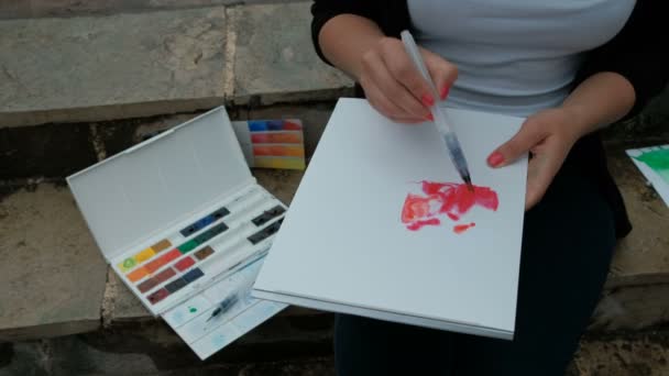 Genç sanatçı merdiven üzerinde oturur ve suluboya resimler ile boyar. — Stok video