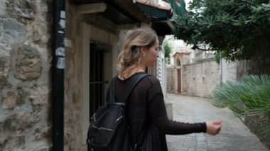 Sarışın genç kadın taş binalar ile sokakta yürüyor.