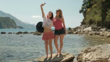 İki kadın alır selfie ayakta kumsalda yaz gününde.