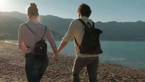 Een man en een vrouw draait op het strand hand in hand bij zonsondergang. — Stockvideo