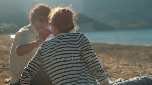 La pareja amorosa se sienta en la playa de arena al atardecer . — Vídeos de Stock