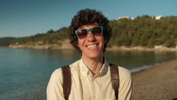 Portrait of a cheerful curly man in stylish sunglasses on the beach. — Stock Video