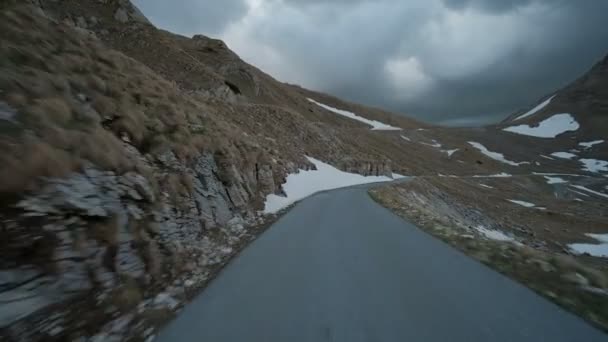 Automobile quickly rides on country road along rocks and dense tamped snow in autumn afternoon. — Stock Video
