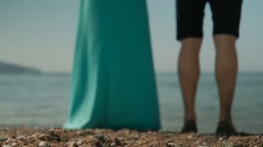 Sahilde duran el ele tutuşarak uzun elbiseli kadın ve erkek. Ellerini tutun