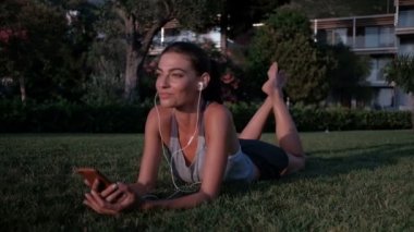 Kadın kulaklık telefon ile müzik dinlemek çim üzerinde yalan.