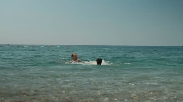 Young man with little daughter bathing in seawater on summer day. — Stock Video