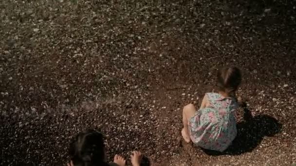 Two little girls sitting on shore of lake with backs outdoors — Stock Video