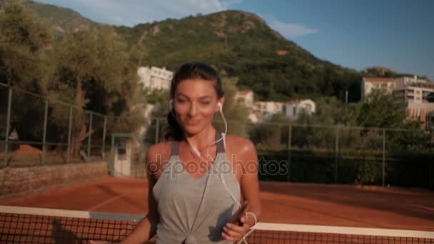 Professional sportswoman jumping on tennis court listening music — Stock Video