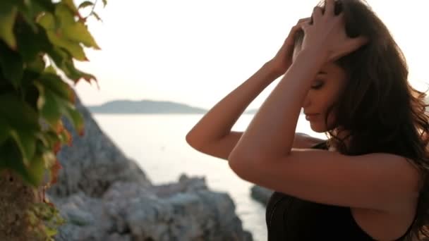 Hermosa mujer endereza el pelo largo sobre un fondo de acantilados puesta de sol — Vídeos de Stock