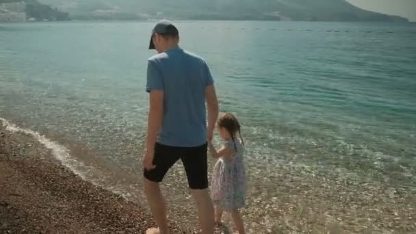 お父さんと彼の娘は、海のビーチに沿って歩いています。. — ストック動画