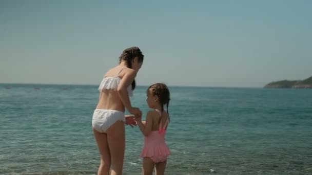 Duas meninas caminham na água pelo mar no dia de verão ao ar livre . — Vídeo de Stock