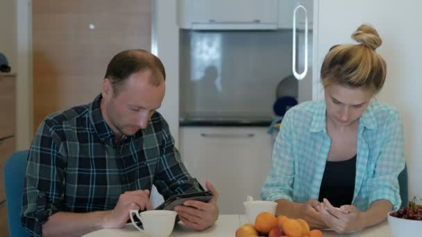 Mann und Frau am Tisch beschäftigen sich schweigend mit der Betrachtung von Gadgets. — Stockvideo