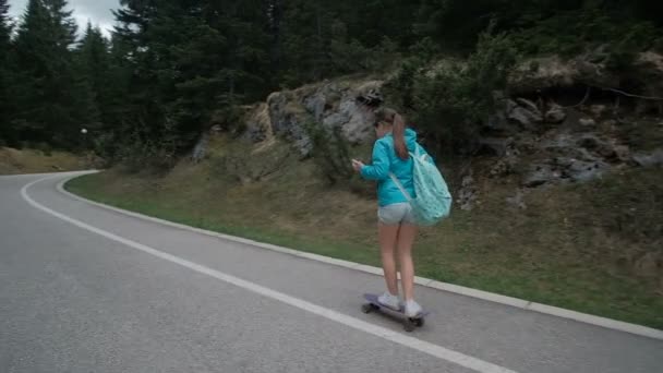 Una chica en un monopatín con una mochila monta en el camino a la vuelta . — Vídeo de stock