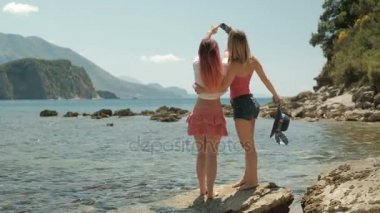 İki kadın selfies sahilde bir kayaya telefonda yapıyor.