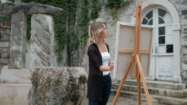 Vacker kvinna står vid ett staffli och hålla en pensel och palett. — Stockvideo