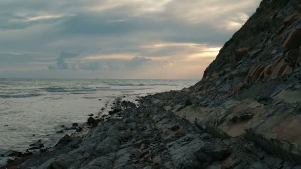 Vid solnedgången vågor försiktigt stänk om steniga stranden. — Stockvideo