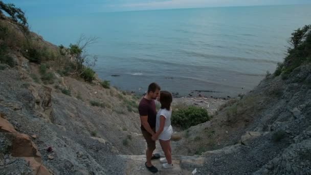 Atractiva pareja besándose de pie en la roca por la orilla del mar en el día de verano al aire libre . — Vídeos de Stock
