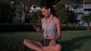 Yeşil çimenlerin üzerinde telefon ile yaz aylarında oturmak müzik dinlemek güzel kadın.