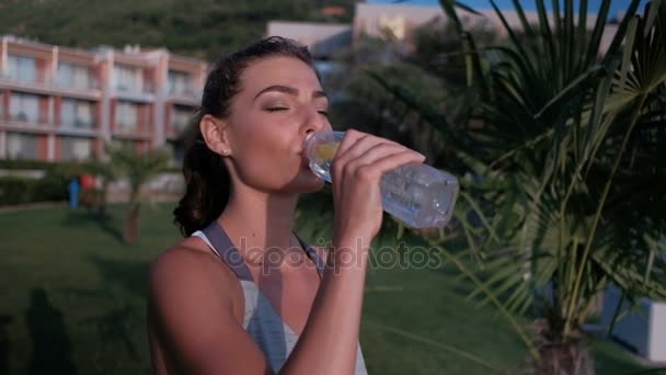 Jovem mulher bebendo água de pé no gramado verde no dia de verão ao ar livre . — Vídeo de Stock