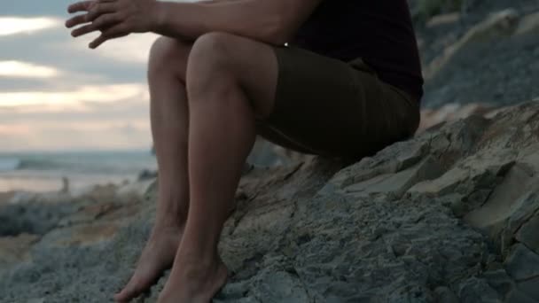 Hombre ven al lago para relajarse sentado en la playa de roca al aire libre — Vídeo de stock