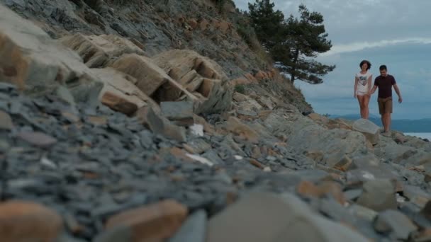 Junge Frau und Mann spazieren an Sommerabend am Strand entlang. — Stockvideo