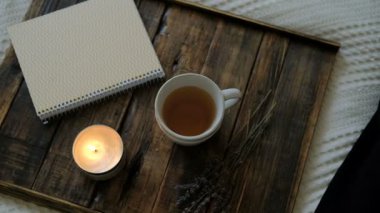 Sıcak çay, oda içinde ahşap tepsi üzerinde yanan mum ve defter.