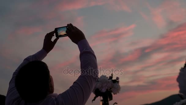 Man in de schemering neemt foto's van kleurrijke hemel op telefoon. — Stockvideo