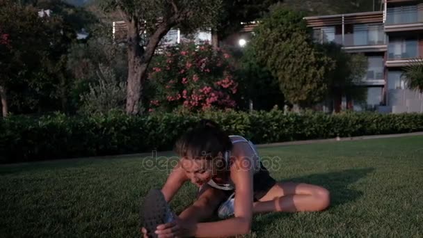 Femme dans un parc sur l'herbe étire ses jambes pendant la forme physique . — Video