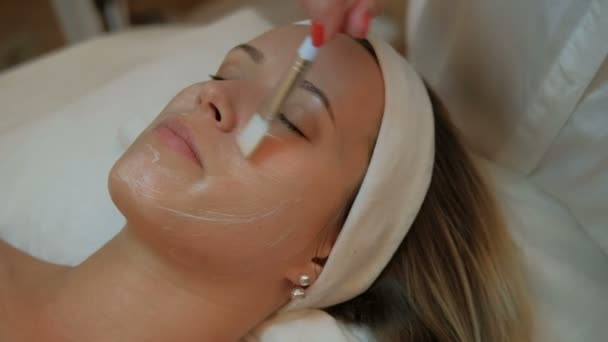 Il cosmetologo esperto mette la maschera su faccia di donna trovante in salone di centro termale all'interno . — Video Stock