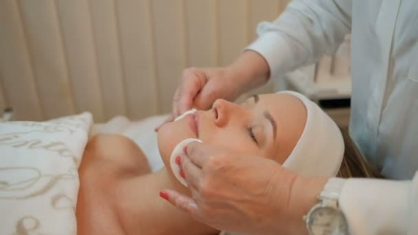 Ervaren schoonheidsspecialist reinigt gezicht van client met katoenen wissers in kliniek. — Stockvideo