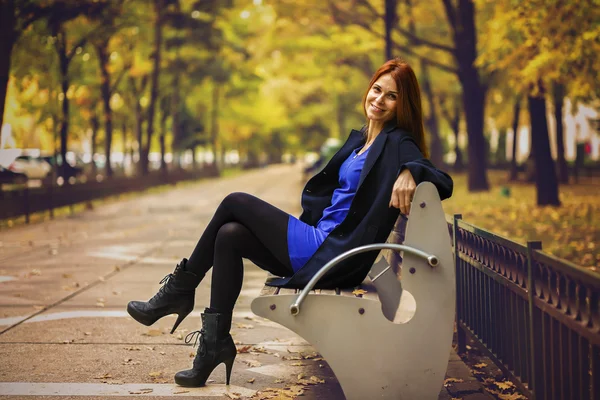 A beautiful and elegant woman on the bench in autumn park — Stock Photo, Image