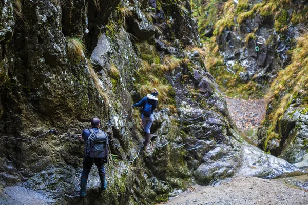 Couple of hikers climbing on safety cables in a gorge above the — Stock Photo, Image