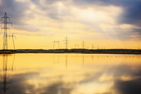 Postes de alto voltaje reflejados en el agua de un lago — Foto de Stock