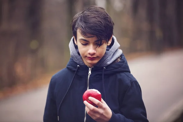 Ung man äta ett rött äpple i parken — Stockfoto