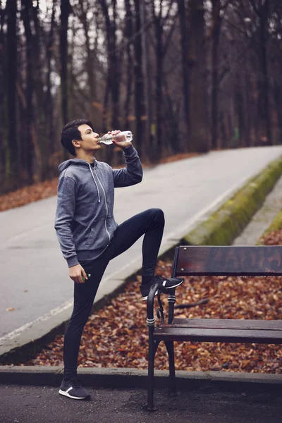 Jovem bebendo água depois de correr no parque — Fotografia de Stock