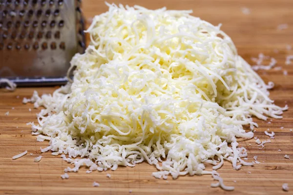 Shredded mozzarella cheese on a cutting board with a grater — Stock Photo, Image
